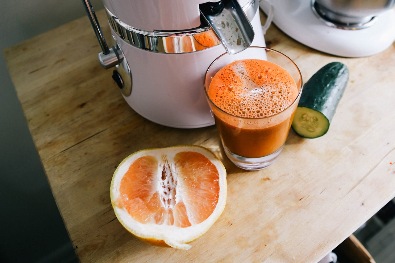 A glass of orange juice on a wooden table with a juicer, half an orange, and a cucumber, representing Solo Product eCommerce category