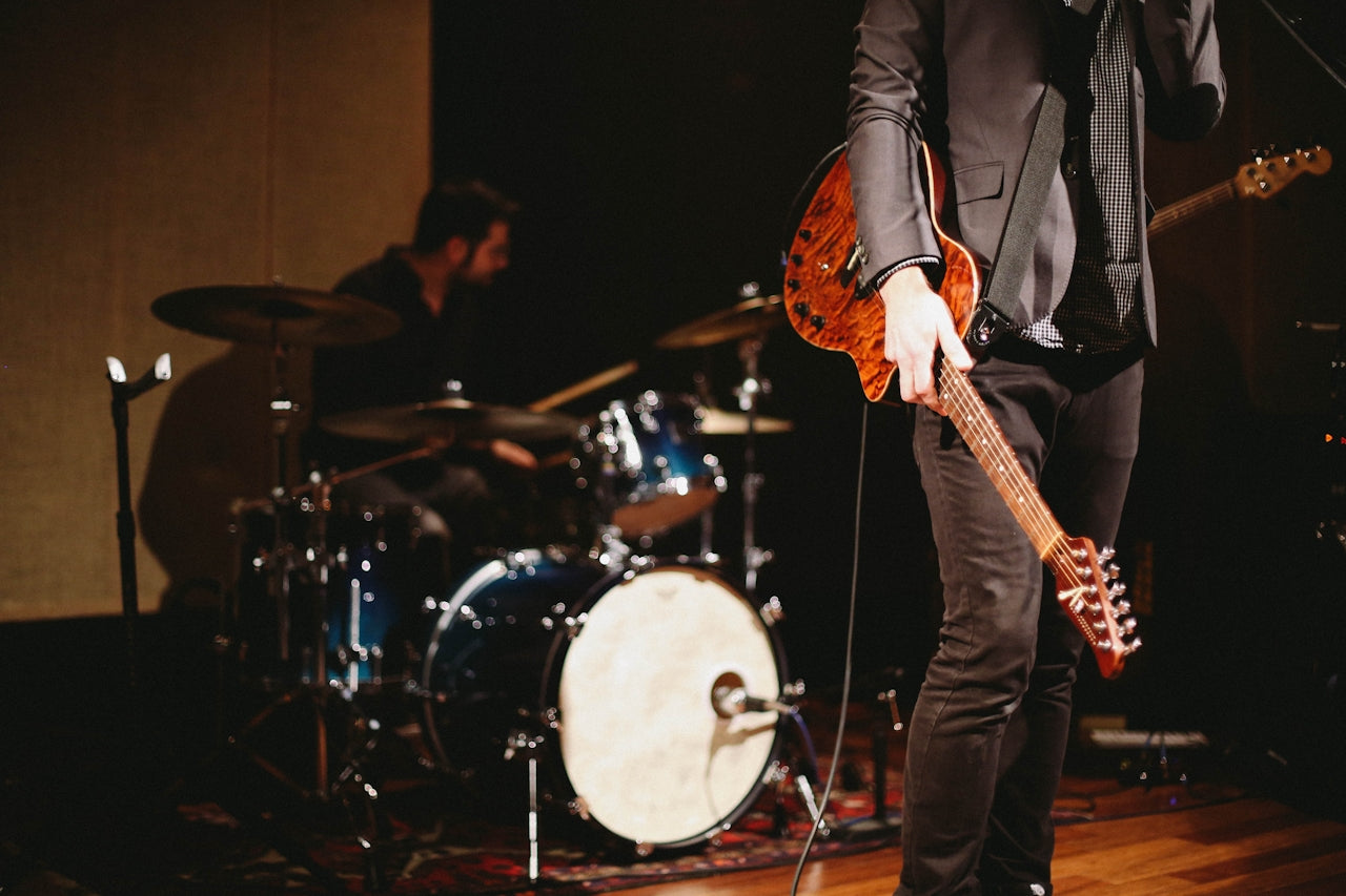 Musicians performing on stage playing guitar with a drum set in the background
