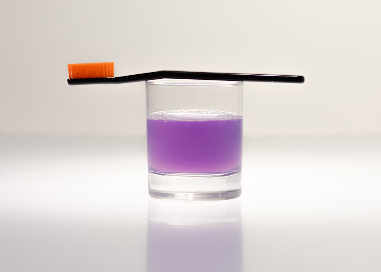 Toothbrush resting on a glass of purple mouth rinse representing Quip and other subscription and CPG ecommerce categories